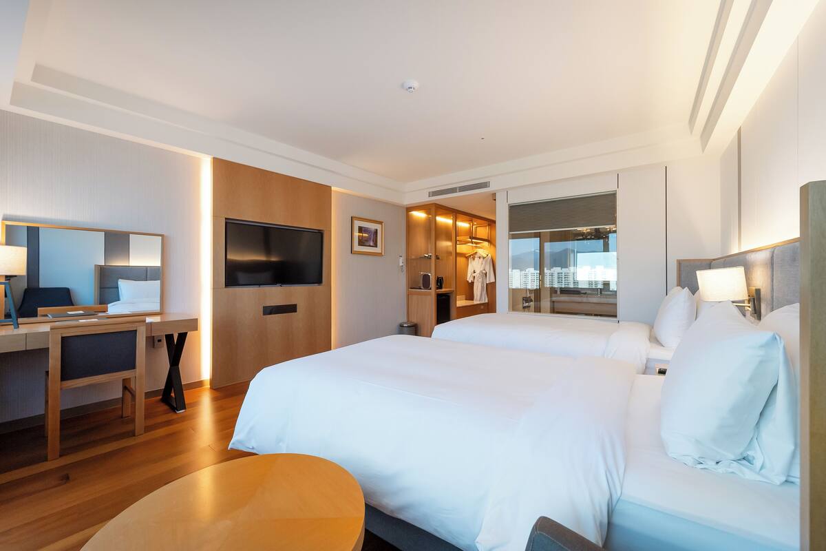 A hotel room with two beds, a desk, a TV, and a view of the city.