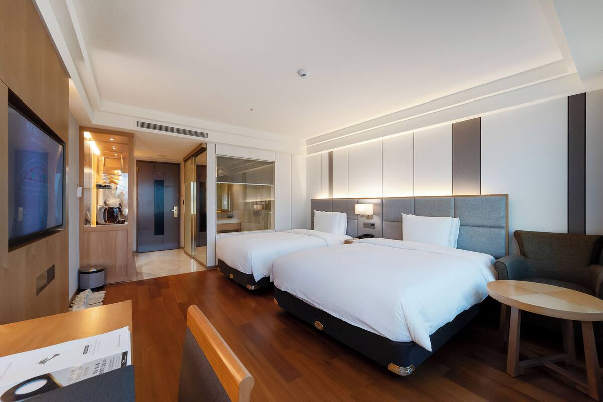 A hotel room with two beds, a TV, a desk, and a small table.