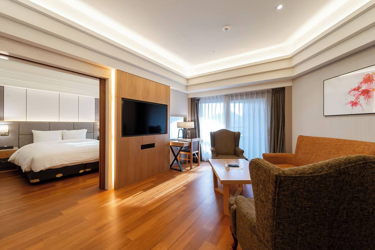 A modern hotel room with a bed, a desk, a TV, and a sofa.