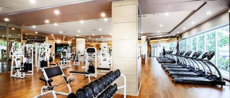 Un gimnasio moderno con máquinas de cardio, equipo de levantamiento de pesas y piso de madera.