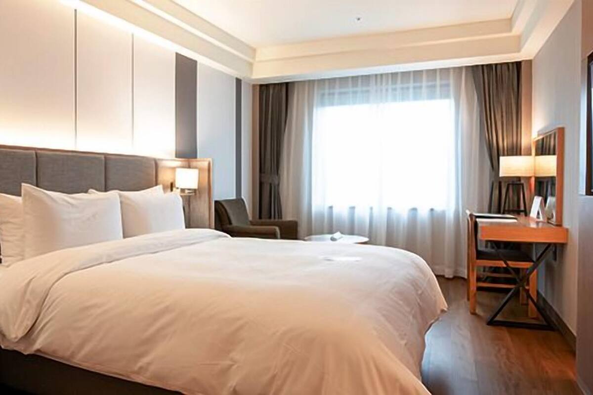 A hotel room with a large bed, bedside tables, a desk, and a large window with curtains.