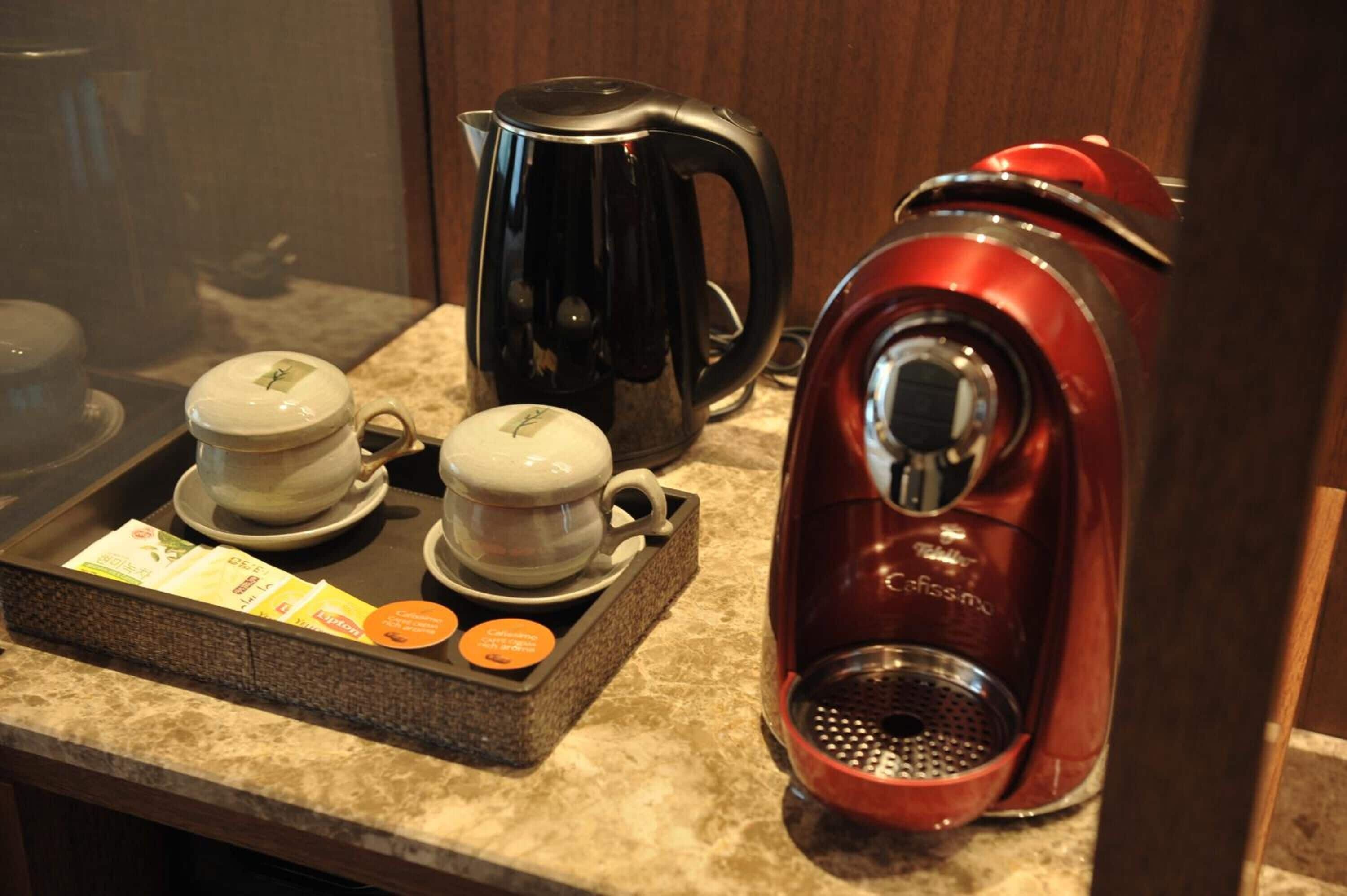A coffee station with a black and red coffee maker, two cups, and a tray with coffee pods.