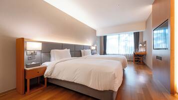 Una habitación de hotel moderna con una cama grande, mesitas de noche, un escritorio y un ventanal amplio.