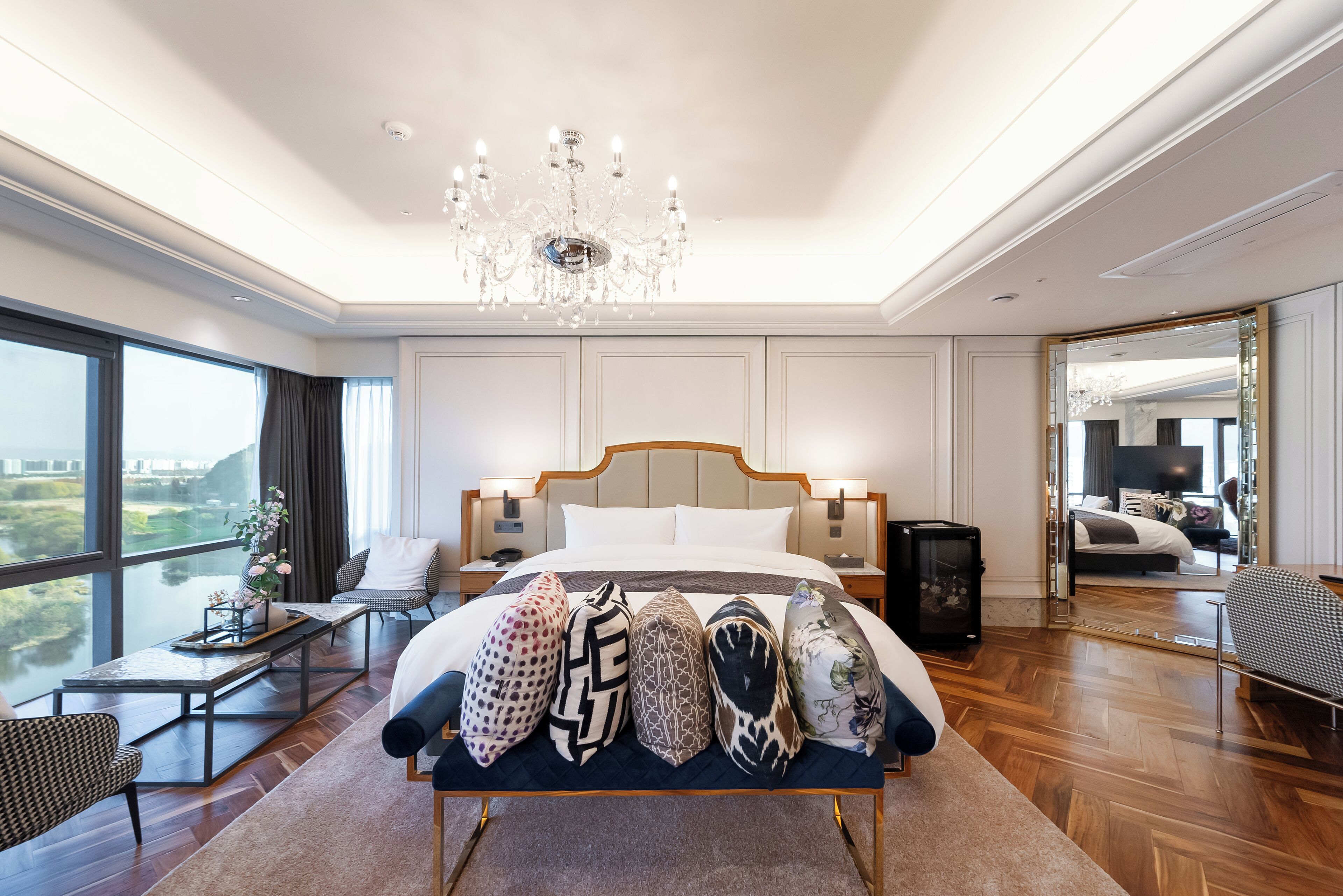 A spacious bedroom with a large bed, a chandelier, and a view of the outdoors.
