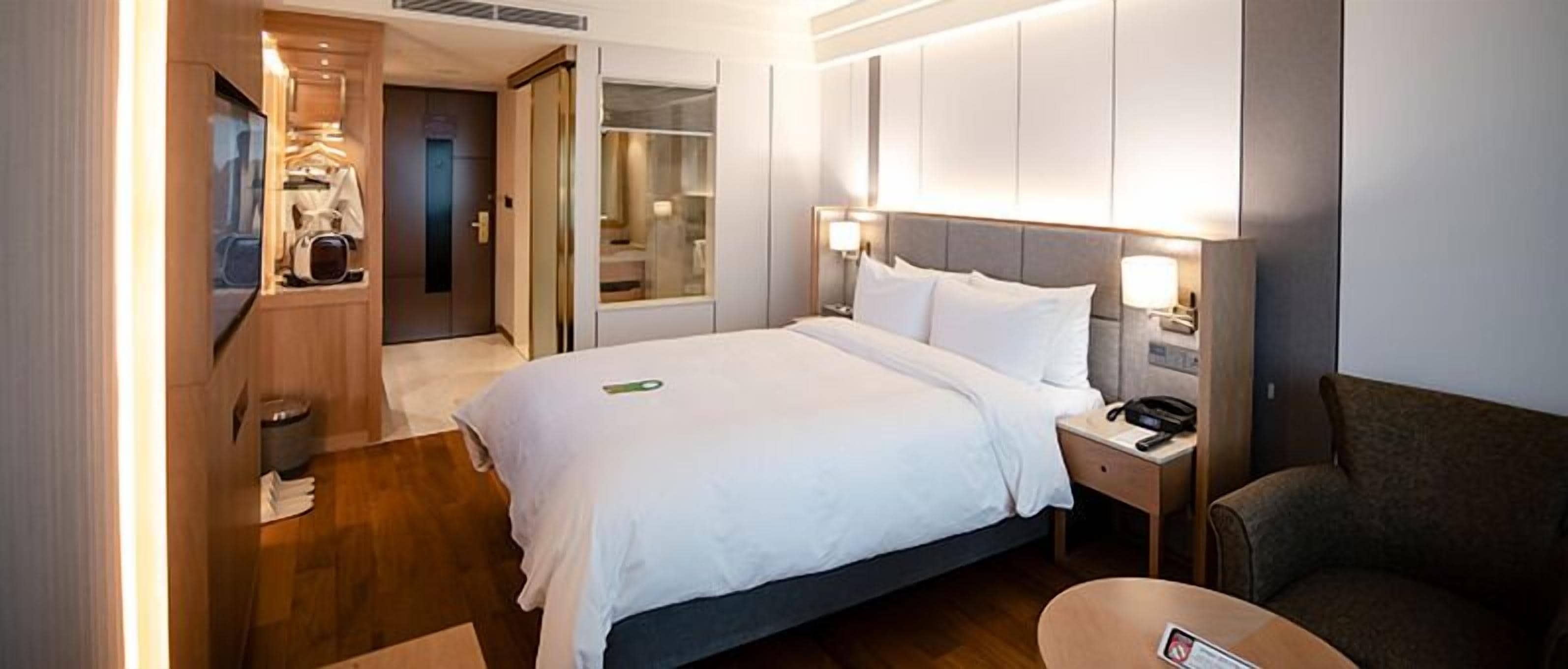 A hotel room with a bed, bedside table, lamp, and a chair.