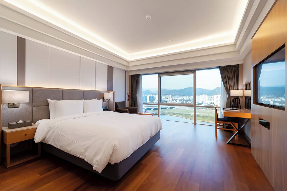A modern hotel room with a large bed, a desk, and a view of the city.