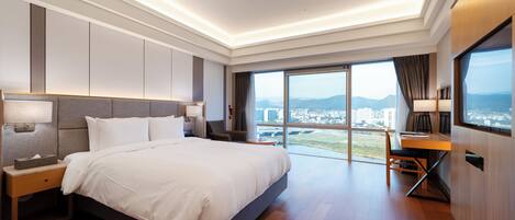 A modern hotel room with a large bed, a desk, and a view of the city.