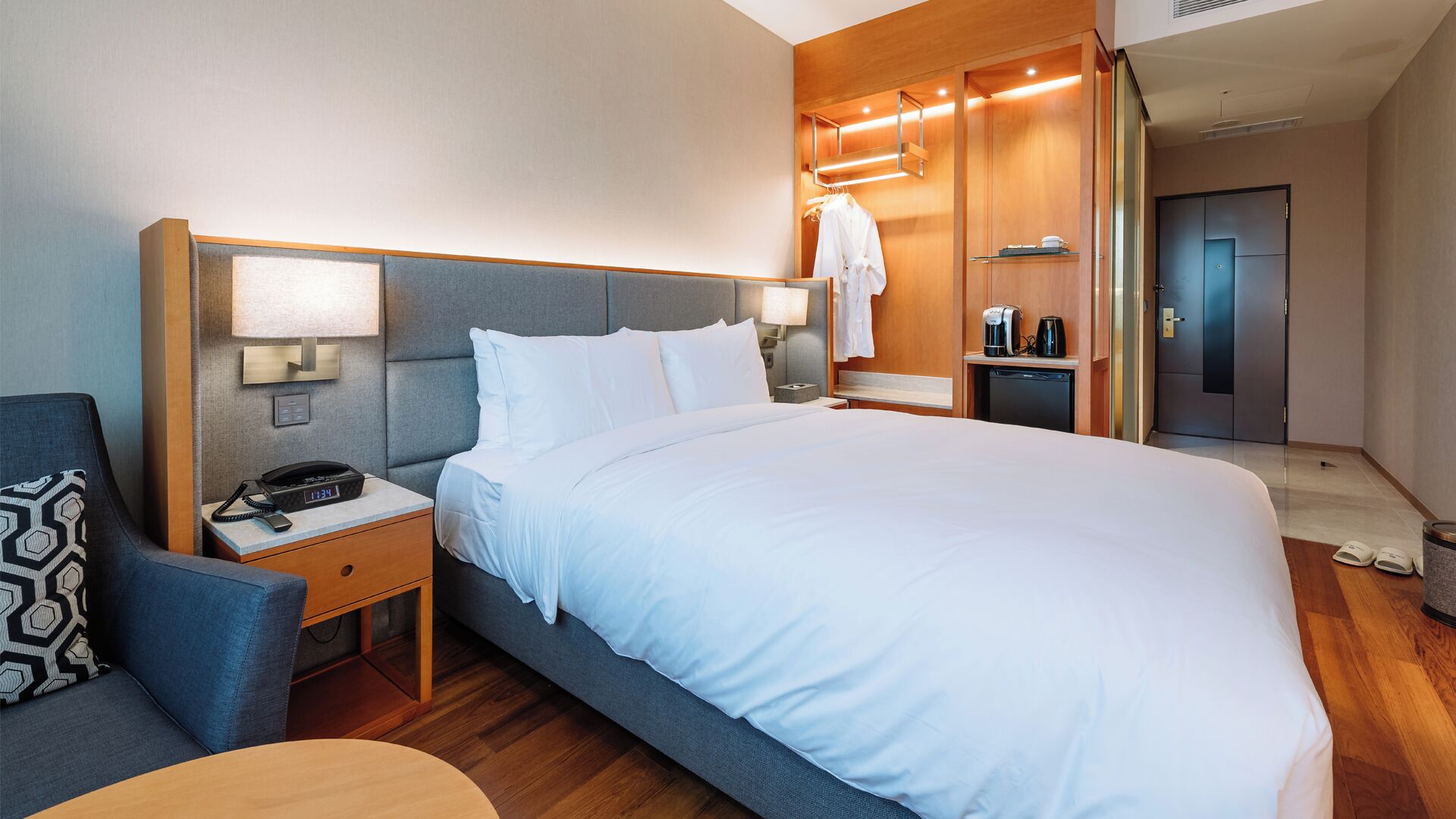 Habitación de hotel con una cama grande, una mesita de noche con teléfono, una silla, un escritorio y un armario.