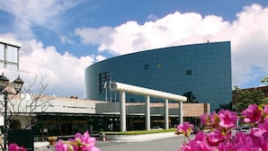 A modern building with a curved facade, large windows, and a prominent cylindrical structure in front.