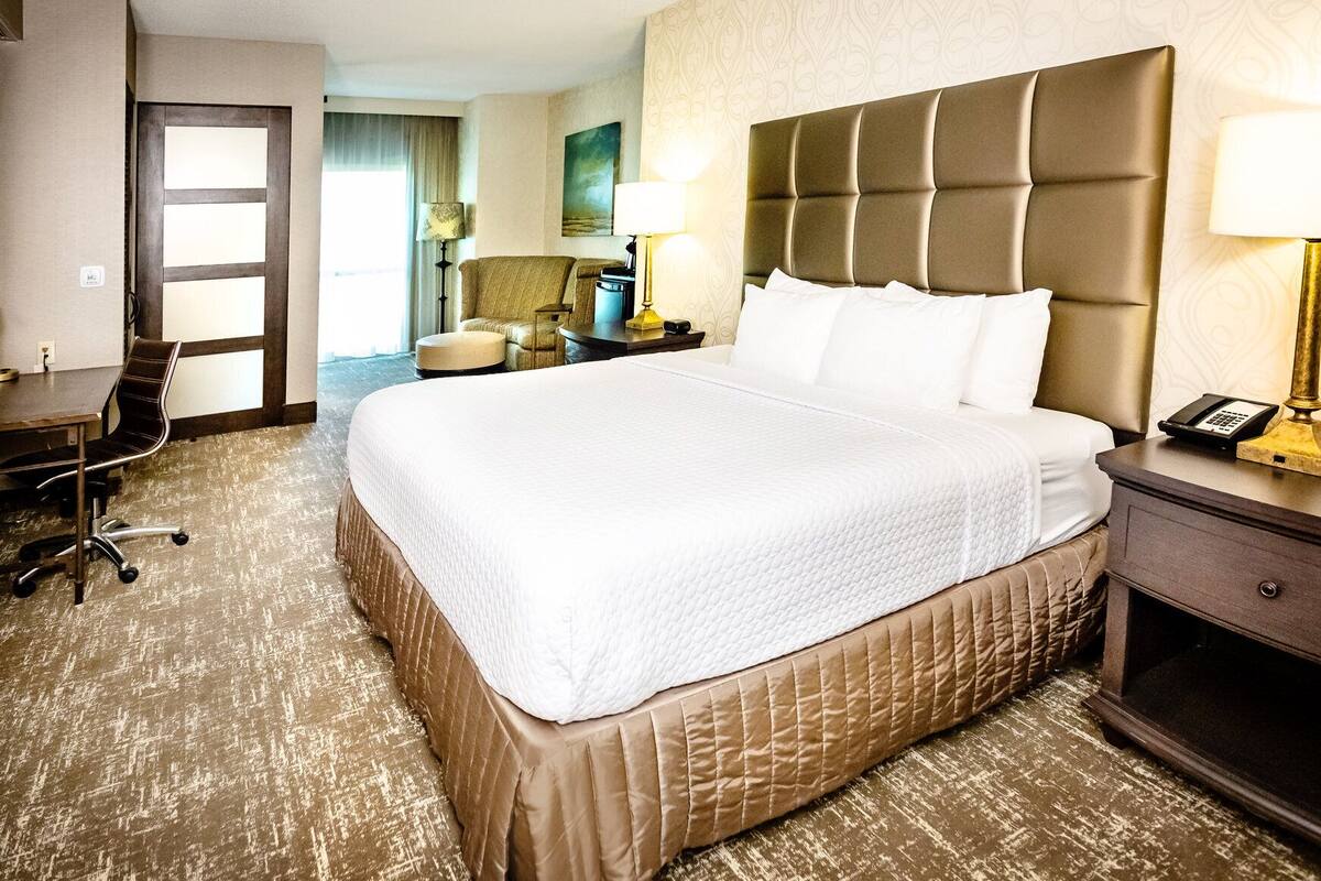 Una habitación de hotel con una cama grande, un escritorio, una silla, una lámpara y un teléfono en la mesita de noche.