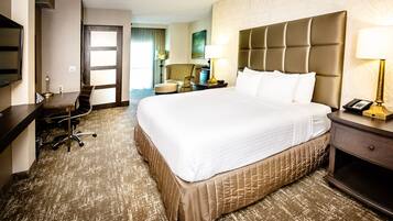 A hotel room with a large bed, a desk, a chair, a lamp, and a telephone on the nightstand.