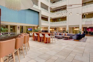 A spacious lobby with a central bar area, multiple seating options, and a high ceiling with hanging lights.
