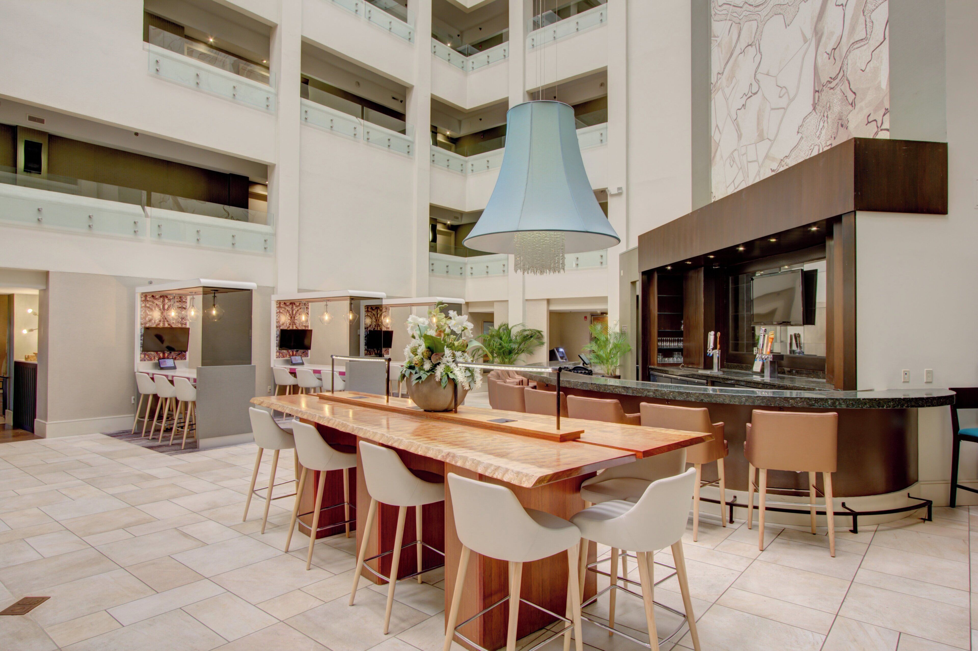 A spacious indoor area with a long wooden table surrounded by chairs, a bar area with a blue pendant light, and a kitchen with a large island.