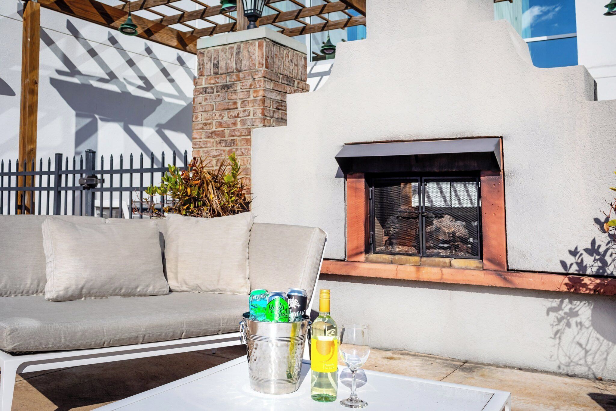 A patio area with a white sofa, a metal table with a drink, and a brick fireplace.