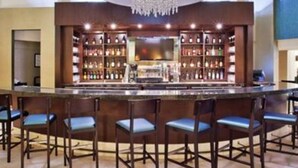 Zona de bar con mostrador alto, varias estanterías llenas de botellas y taburetes.