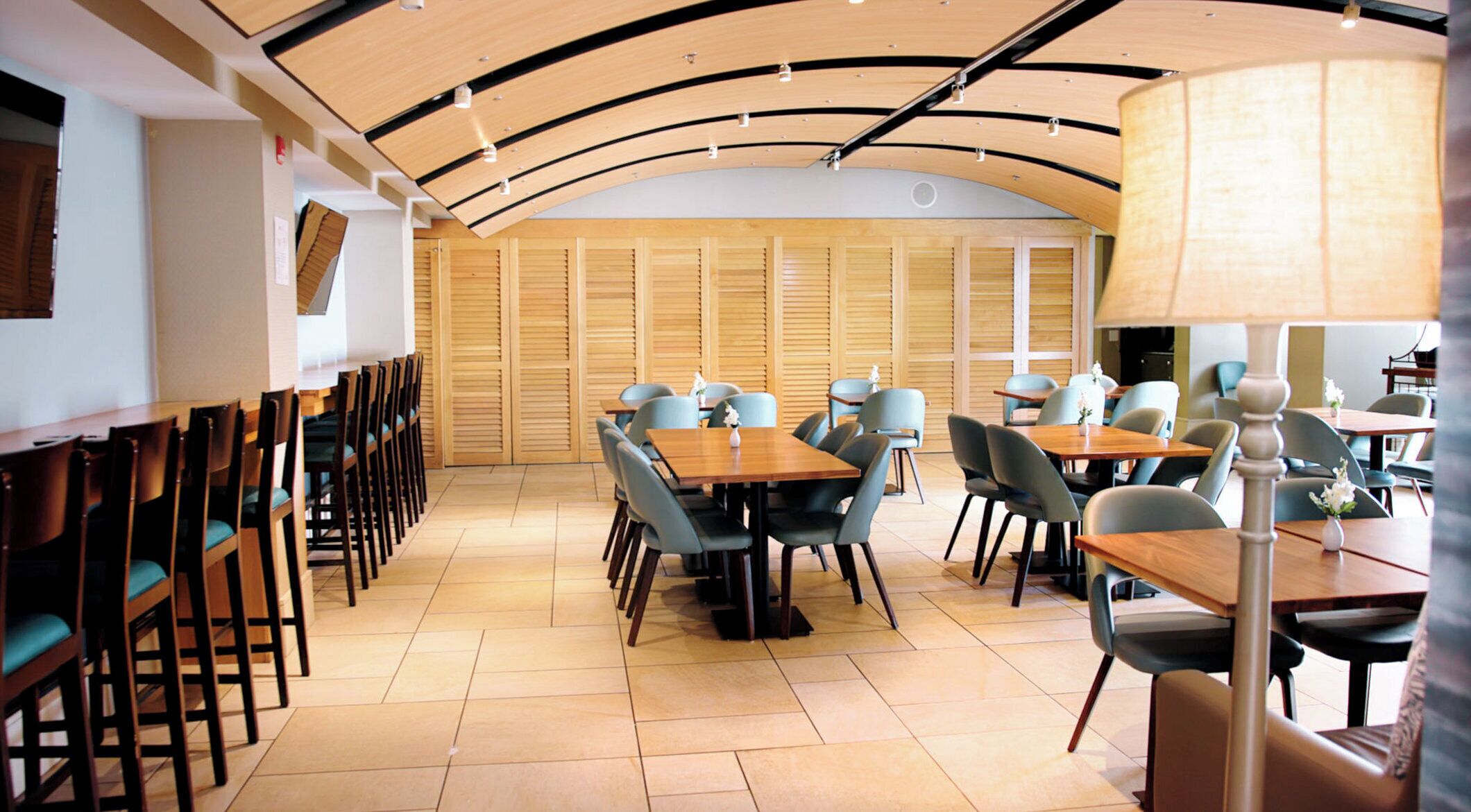 Un comedor con mesas y sillas de madera, techo curvo y piso de baldosas.