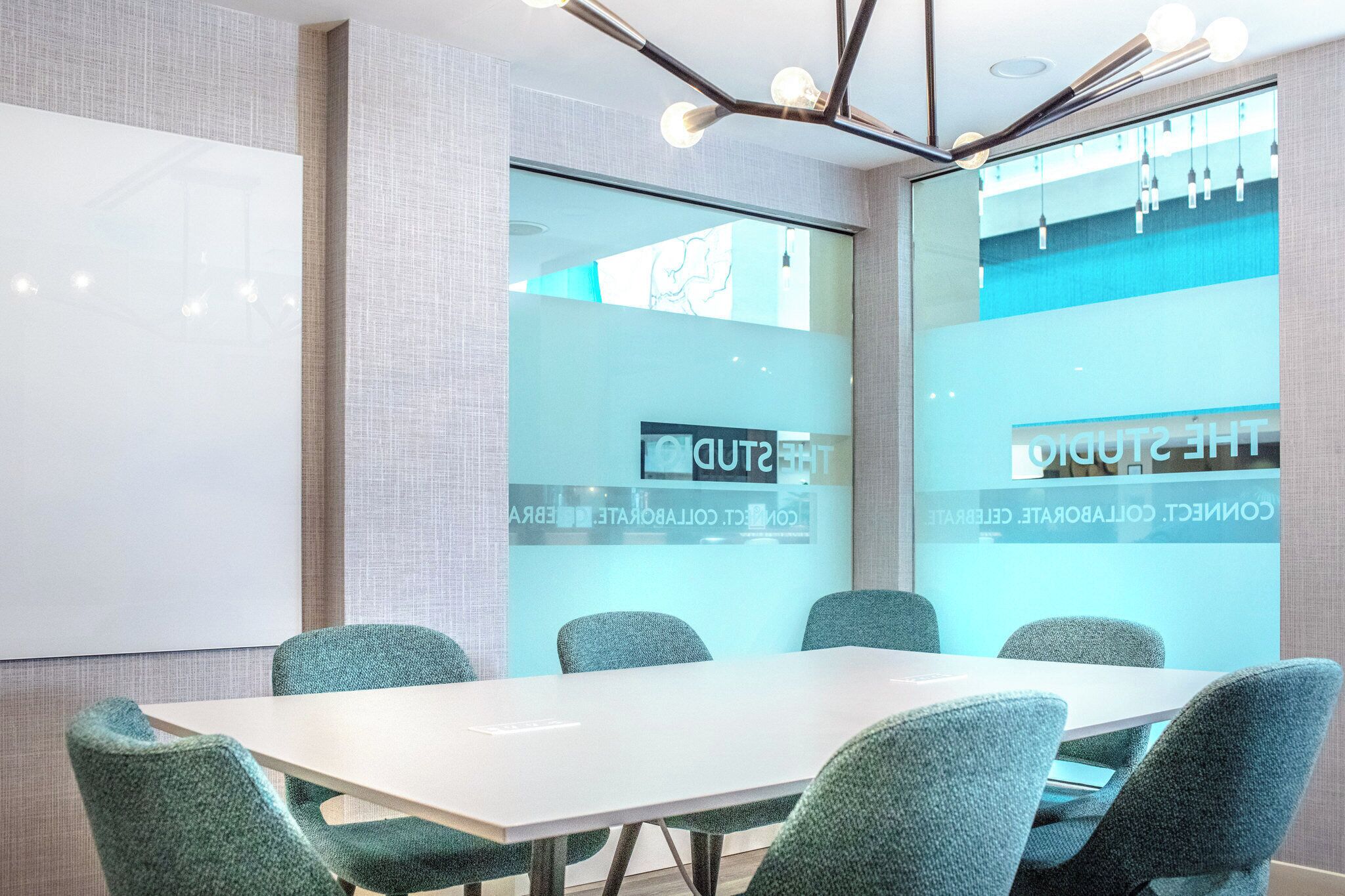 Une salle de conférence avec une table blanche, des chaises de couleur turquoise et une grande fenêtre donnant sur un beau paysage.