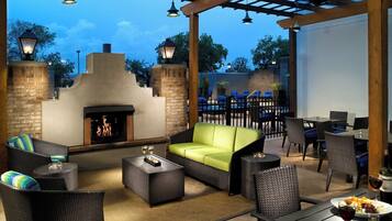 An outdoor patio with a fireplace, wicker furniture, and a pool area.