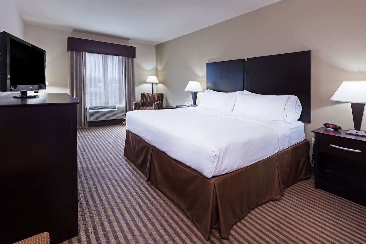 A hotel room with a large bed, a desk with a computer, a chair, and a window with curtains.