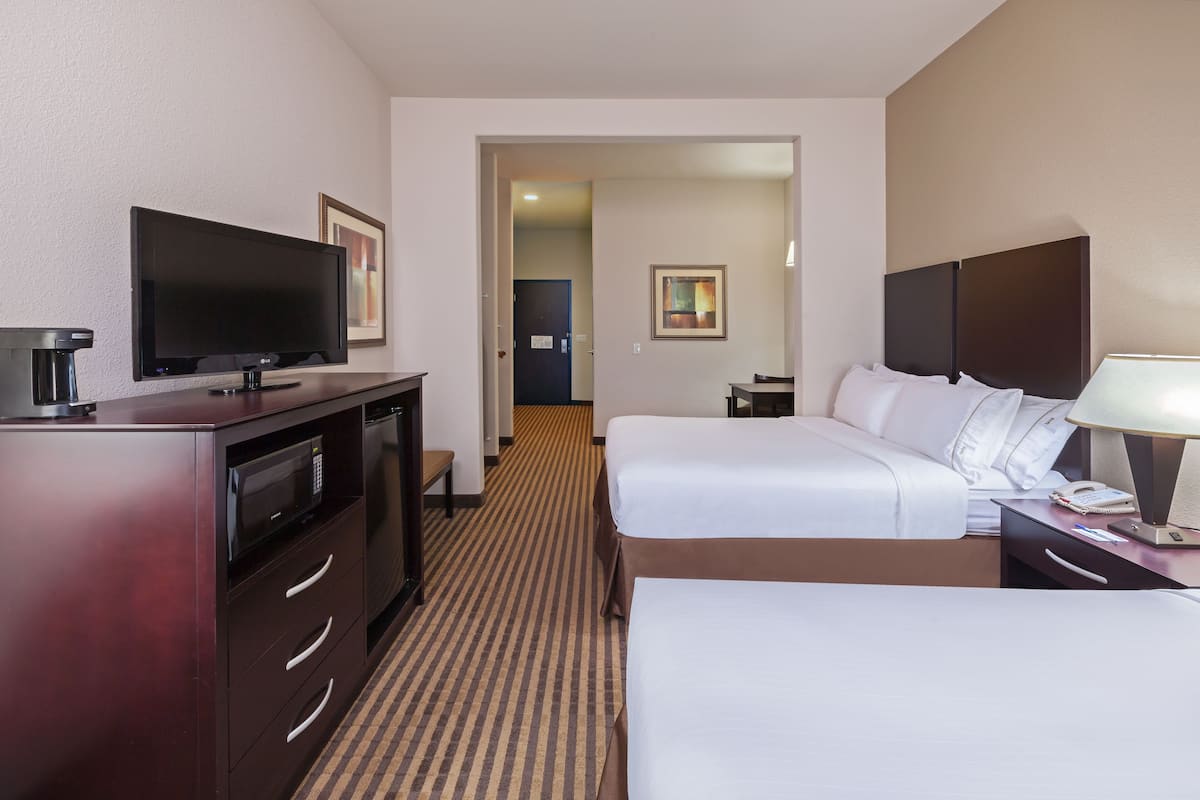 A hotel room with a flat-screen TV, a desk with a lamp, two beds, a microwave, and a coffee maker.