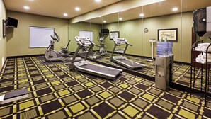 Un gimnasio con cintas de correr, elíptica y dispensador de agua.