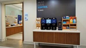 A coffee station with multiple coffee makers, a sign stating "MUST. HAVE. COFFEE.", and a counter with various coffee-related items.