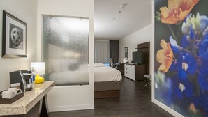 Une chambre d’hôtel avec un lit, un bureau doté d’une lampe, une machine à café et un tableau encadré au mur.