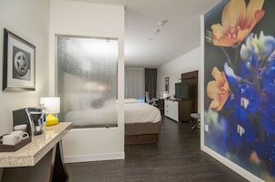 A hotel room with a bed, a desk with a lamp, a coffee maker, and a framed picture on the wall.