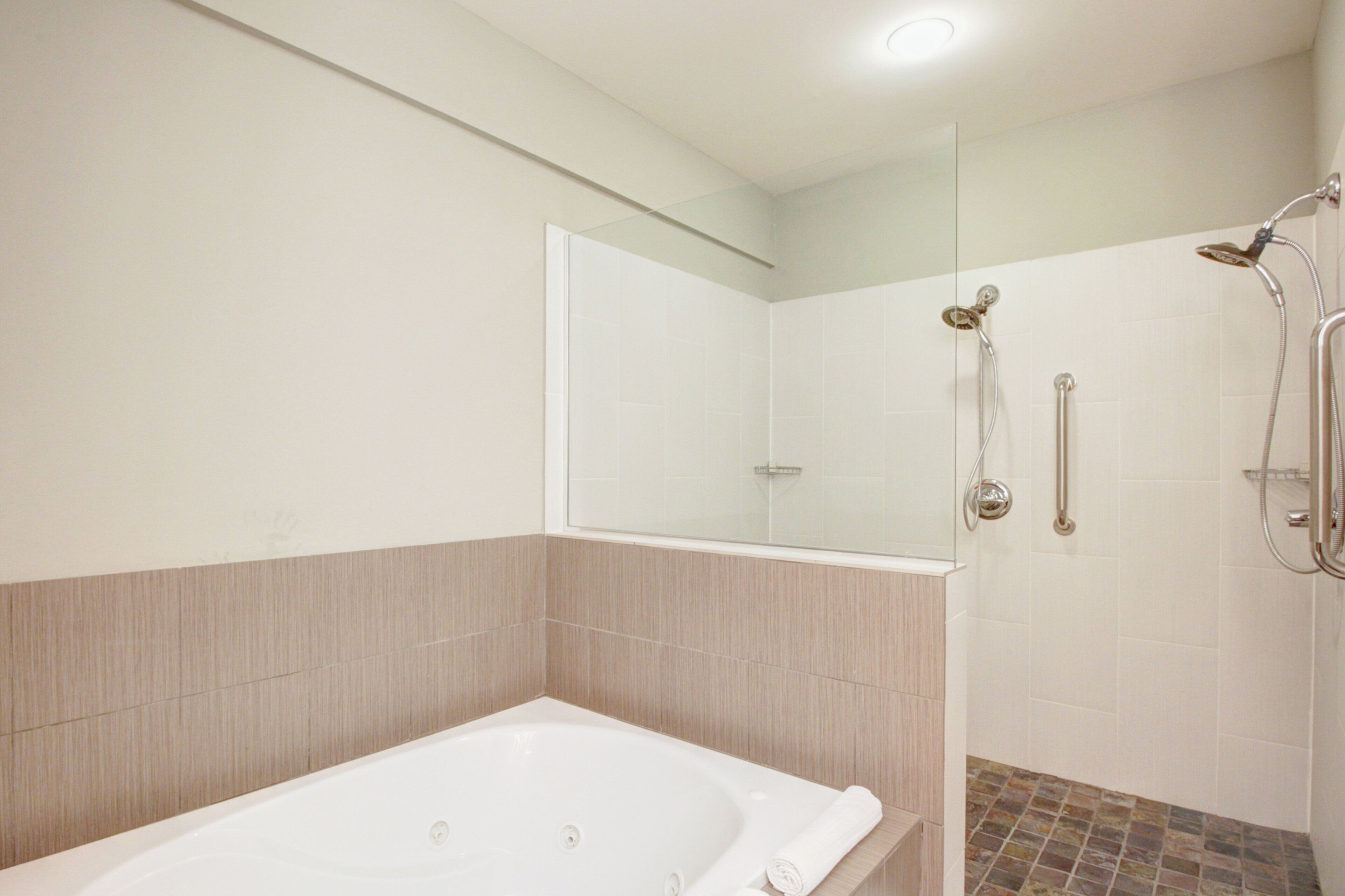 A bathroom with a bathtub, a shower with a handheld showerhead, and a glass-enclosed shower stall.