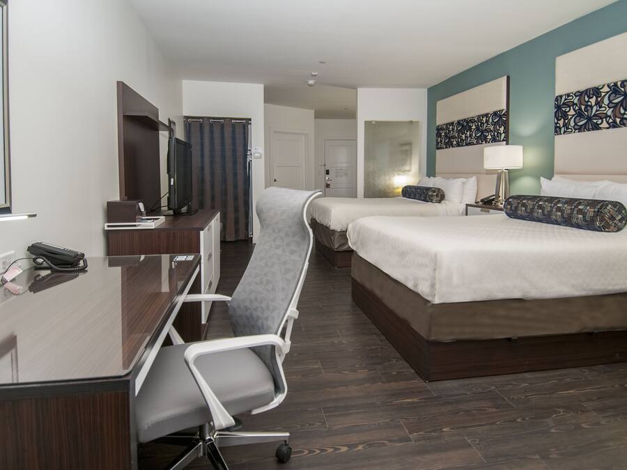 Habitación de hotel con escritorio, dos camas, una silla y televisión.