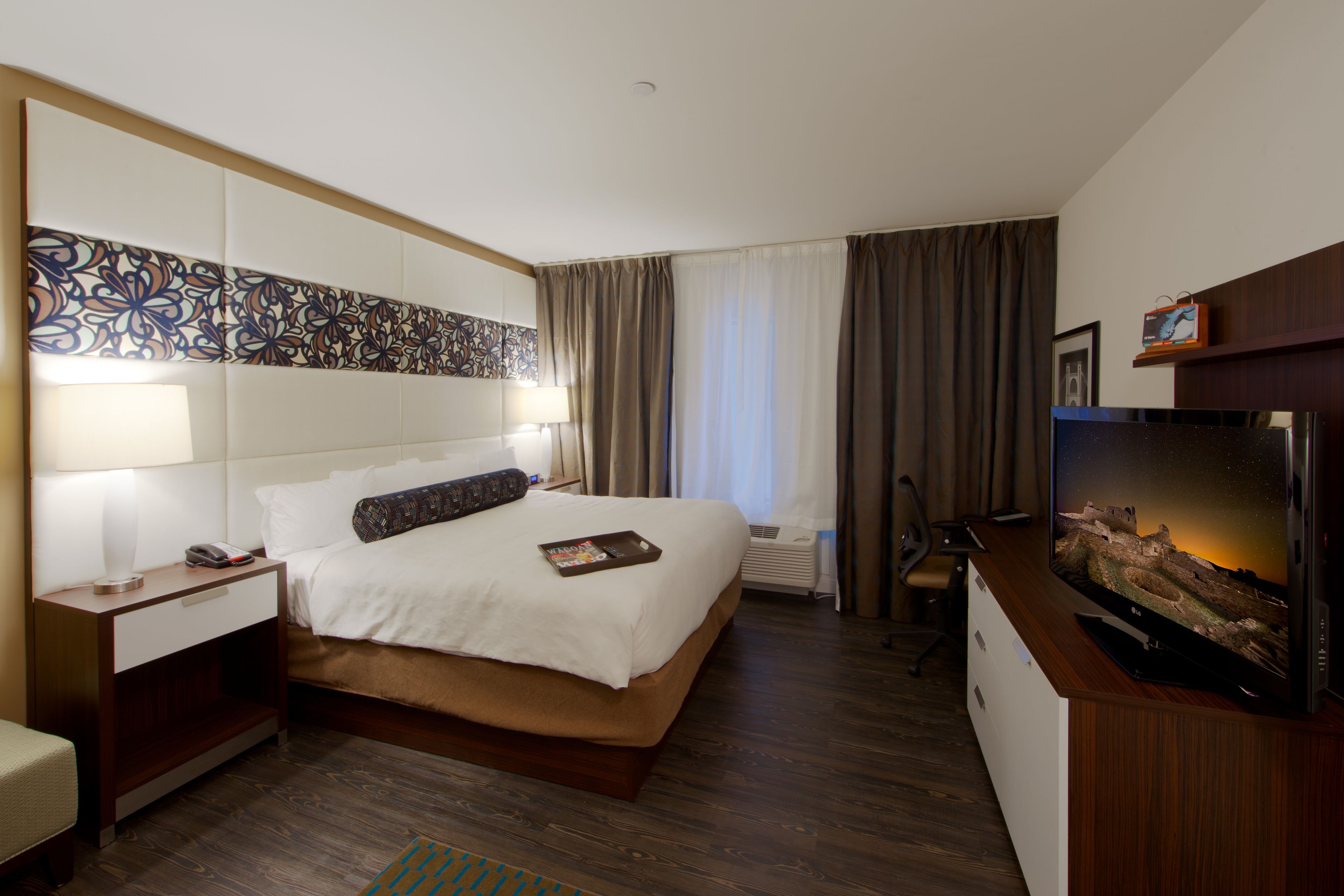 Une chambre d’hôtel avec un grand lit, un bureau équipé d’un ordinateur, une télévision et un panneau décoratif au mur.
