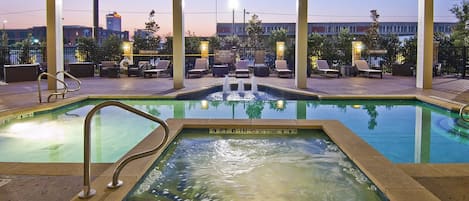 Un área de piscina con sillones de descanso y un jacuzzi, rodeado por un porche cubierto con vistas al horizonte de la ciudad.