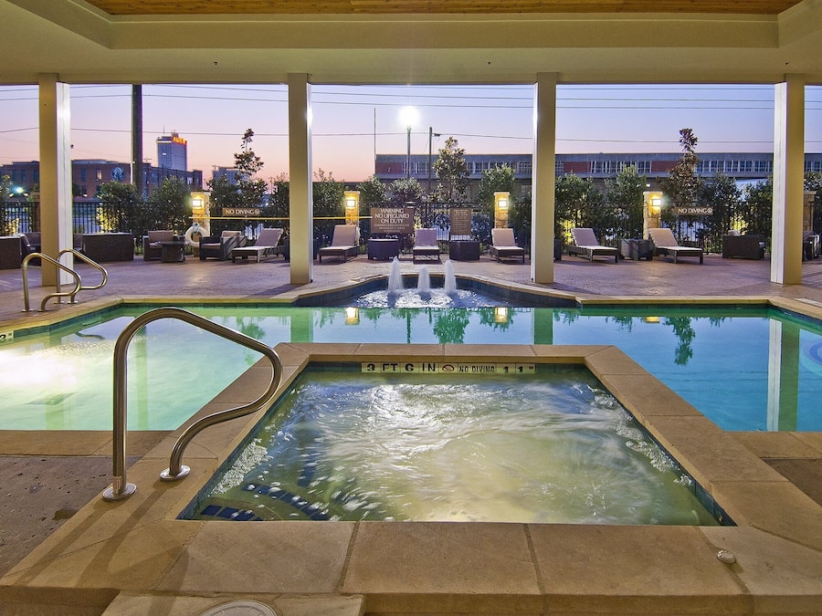 A pool area with lounge chairs and a hot tub, surrounded by a covered patio with a view of the city skyline.