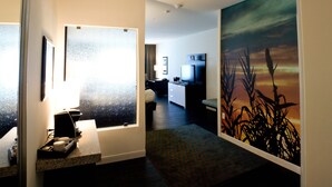 Une chambre d’hôtel équipée d’une kitchenette, d’un lit, d’une télévision et ornée d’un grand tableau représentant un coucher de soleil.