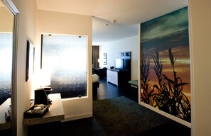 Une chambre d’hôtel équipée d’une kitchenette, d’un lit, d’une télévision et ornée d’un grand tableau représentant un coucher de soleil.