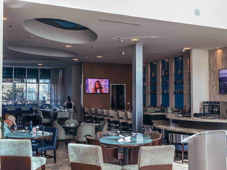 Eine moderne Bar mit Sitzgelegenheiten, einem Fernsehbildschirm und Blick auf die Stadt durch große Fenster.
