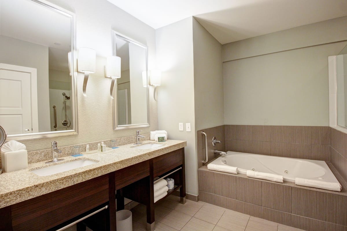 A modern bathroom with a double sink vanity, a large mirror, a walk-in shower, and a standalone bathtub.