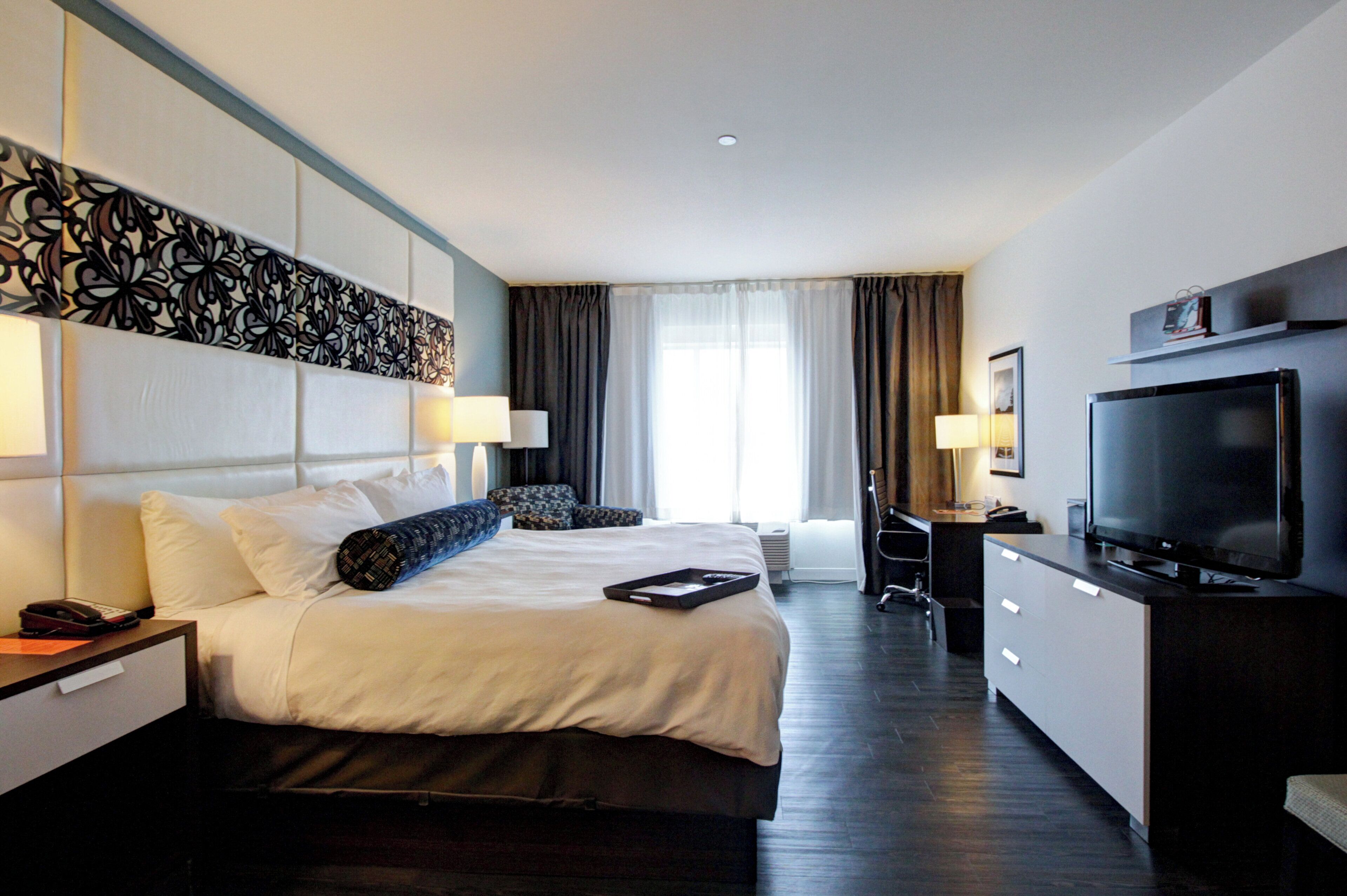 A hotel room with a large bed, a TV, a desk, and a chair.