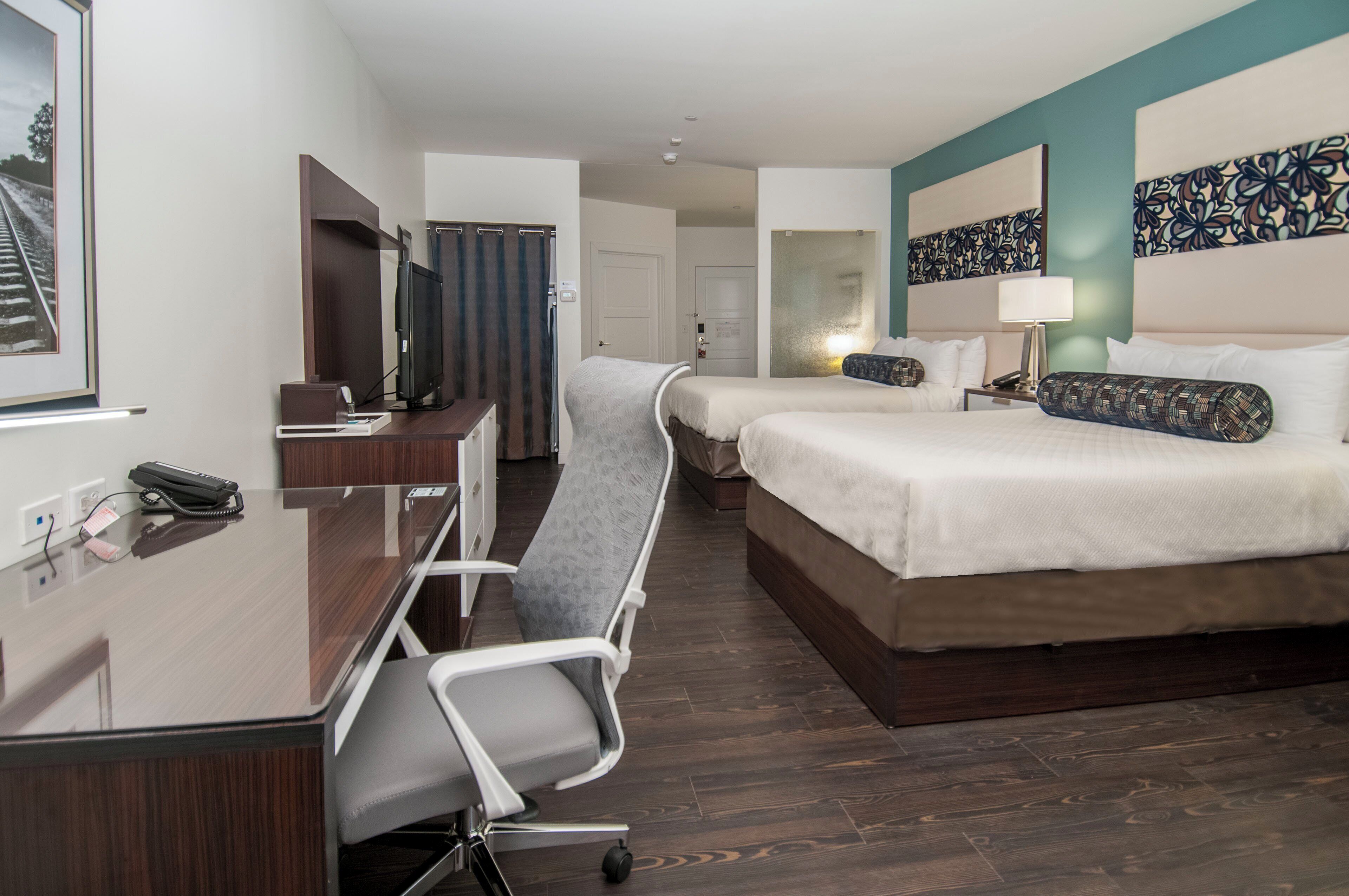 Habitación de hotel con escritorio, dos camas, una silla, televisor y puerta de baño.