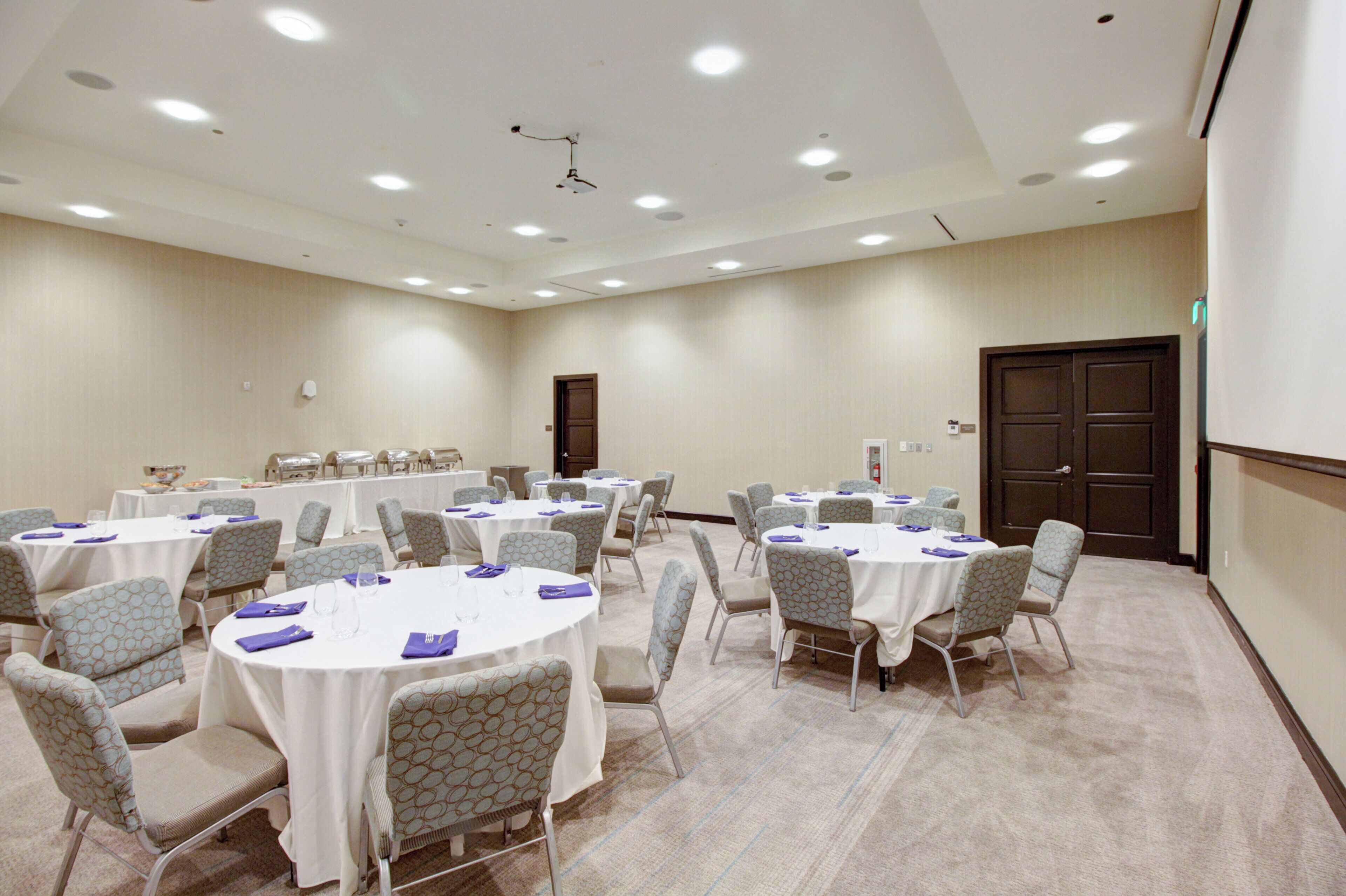 A conference room with round tables, chairs, and a projector screen.