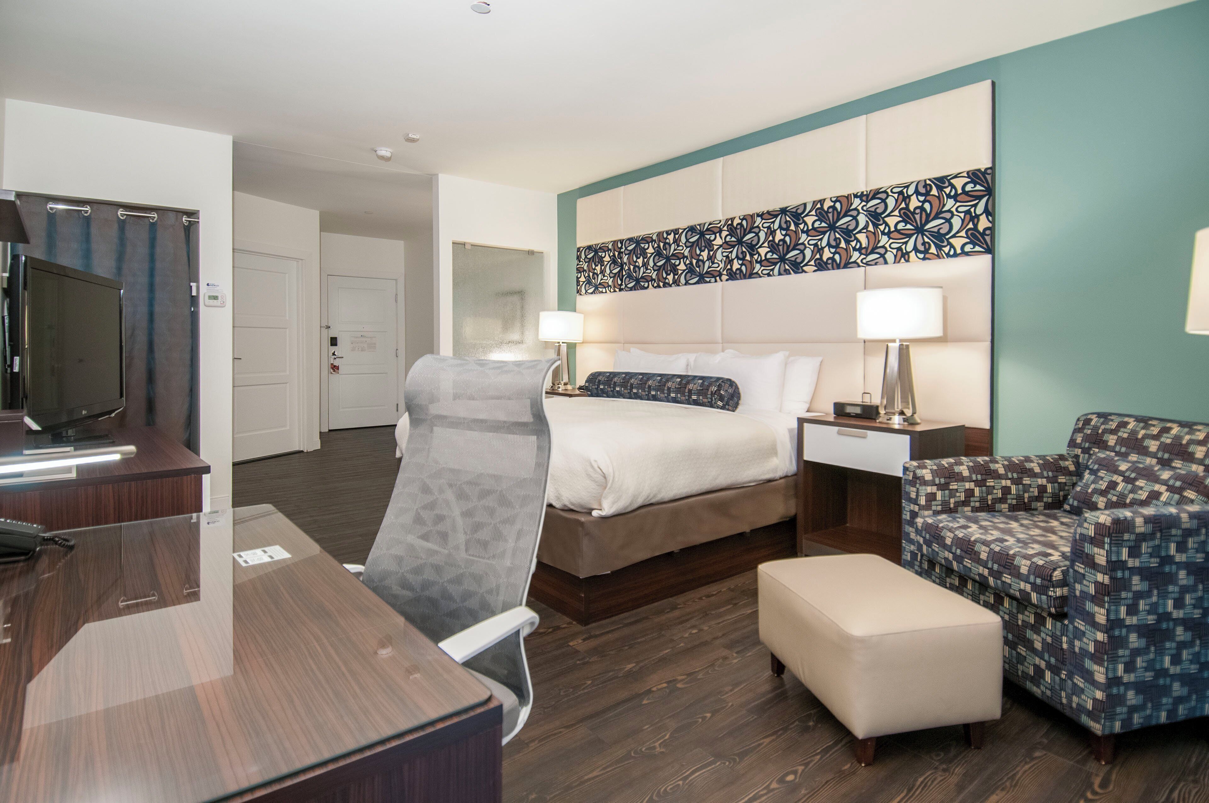 A hotel room with a bed, a desk, a TV, a chair, and a patterned wall.