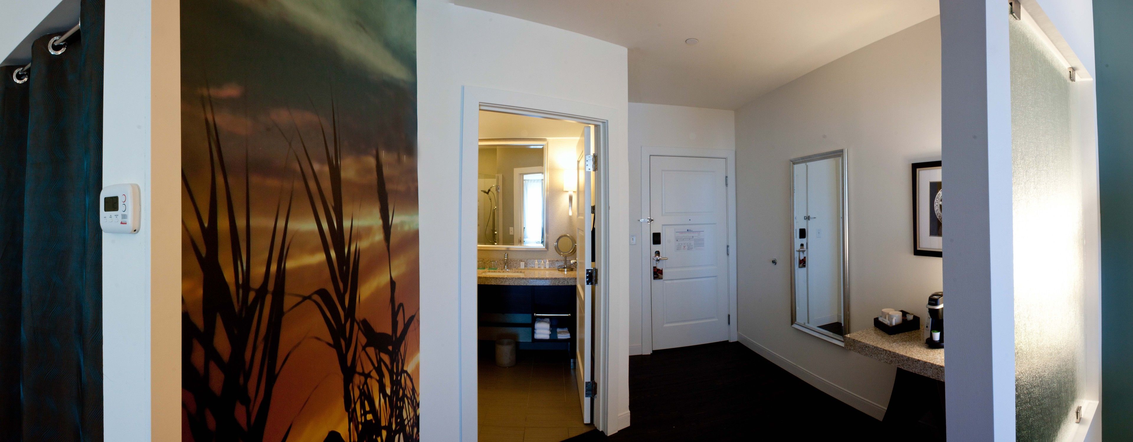 A hallway with a painting, a bathroom with a sink and mirror, and a door leading to another room.