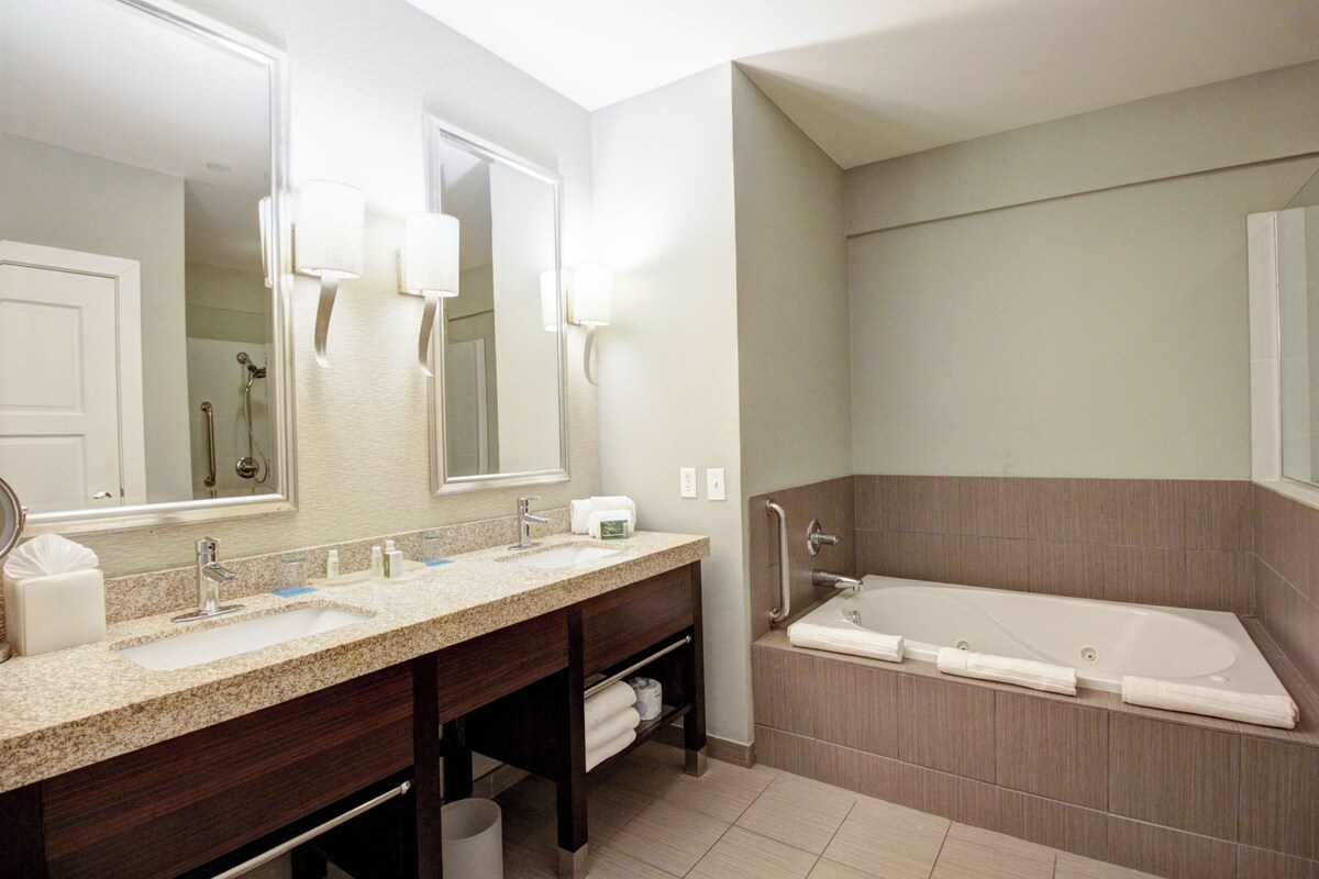 A bathroom with a double sink, a large mirror, a bathtub, and a towel rack.
