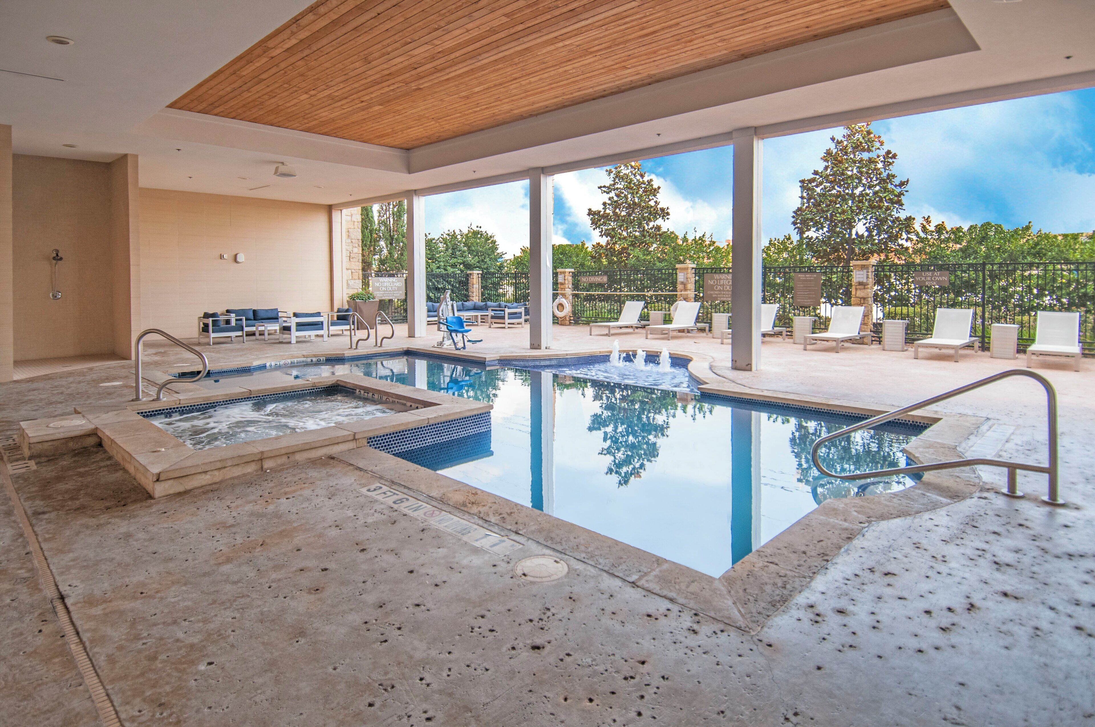 A pool area with a hot tub, lounge chairs, and a view of the outdoors.