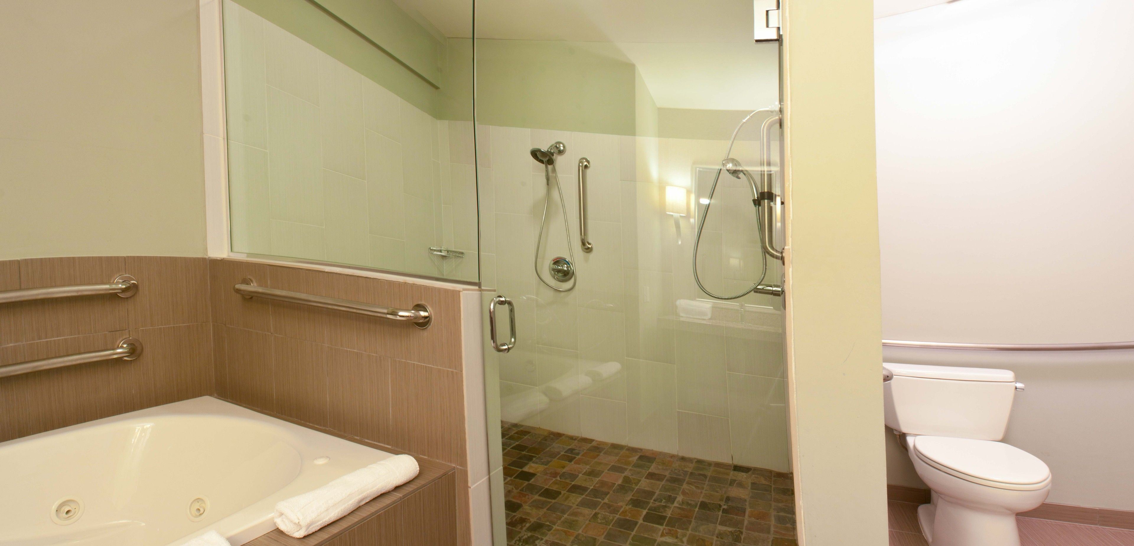 A bathroom with a glass-enclosed shower, a bathtub with grab bars, and a toilet.