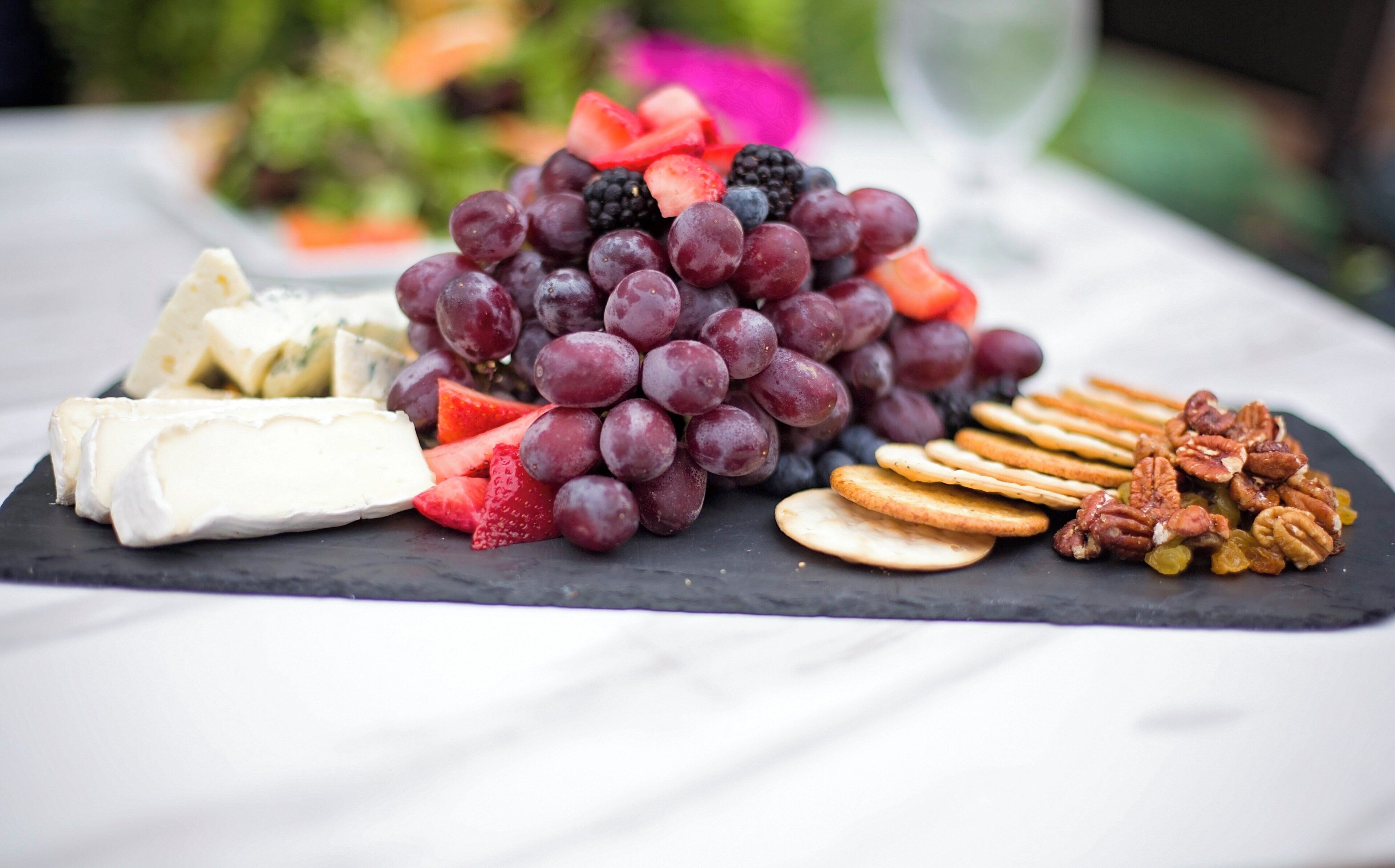 Une planche de charcuterie accompagnée de fromage, de raisins, de fraises, de noix de pécan et de crackers.