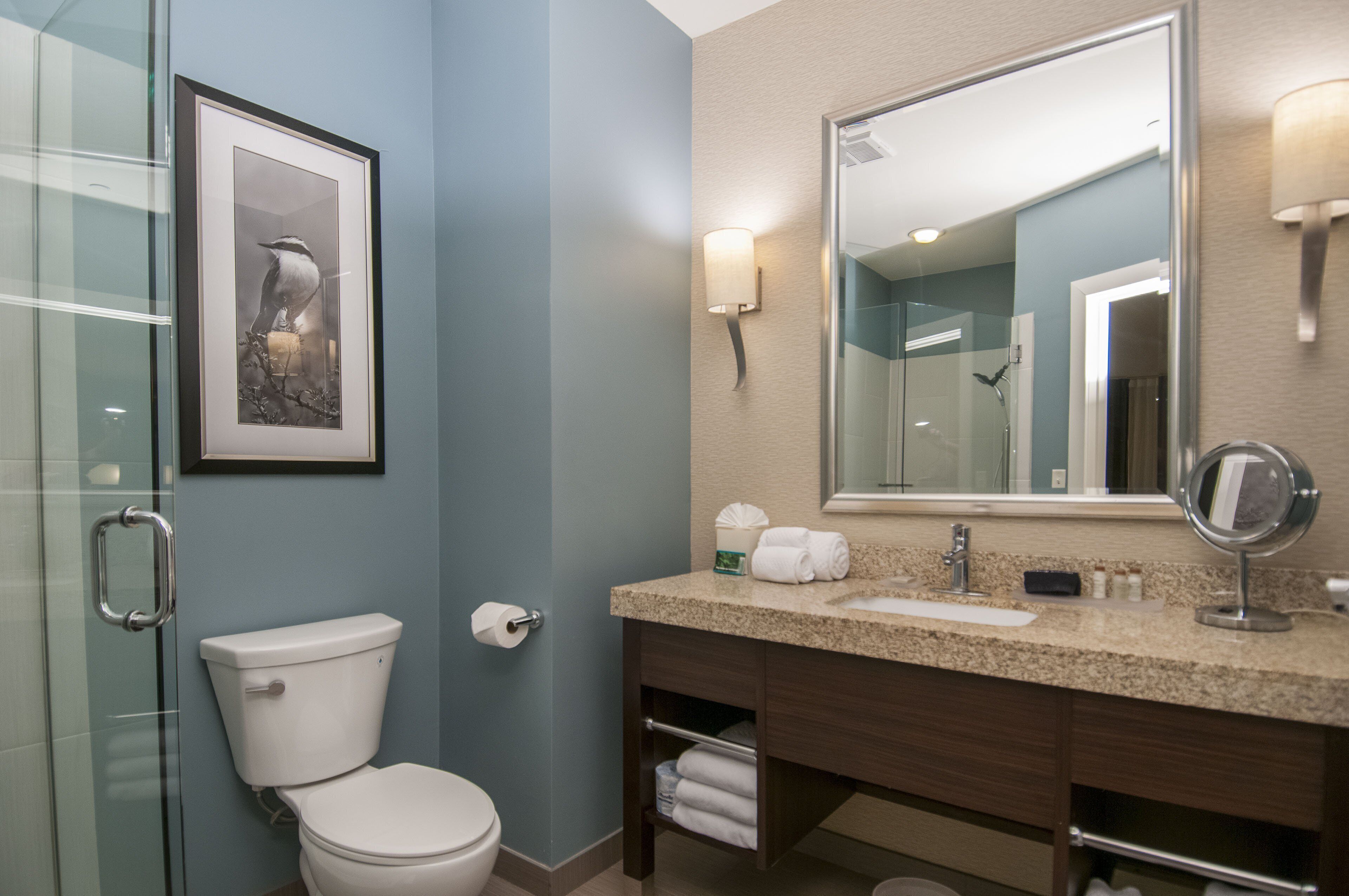 A bathroom with a toilet, sink, vanity, and a framed picture on the wall.