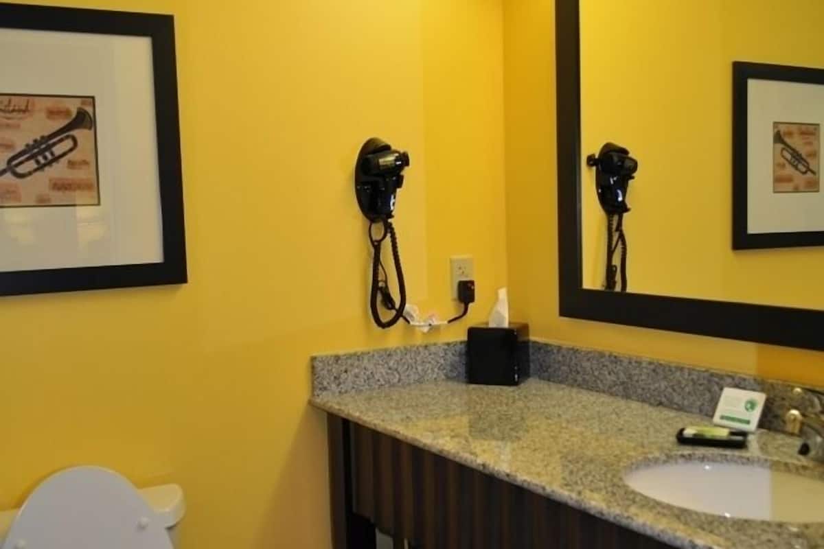 A bathroom with a yellow wall, a white toilet, a sink with a mirror above it, and a towel rack with towels.