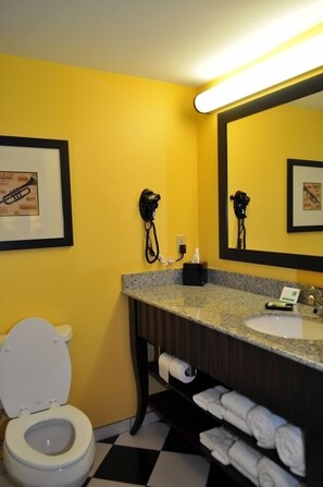 Un baño con una pared amarilla, un inodoro blanco, un lavamanos con un espejo encima y un perchero con toallas.