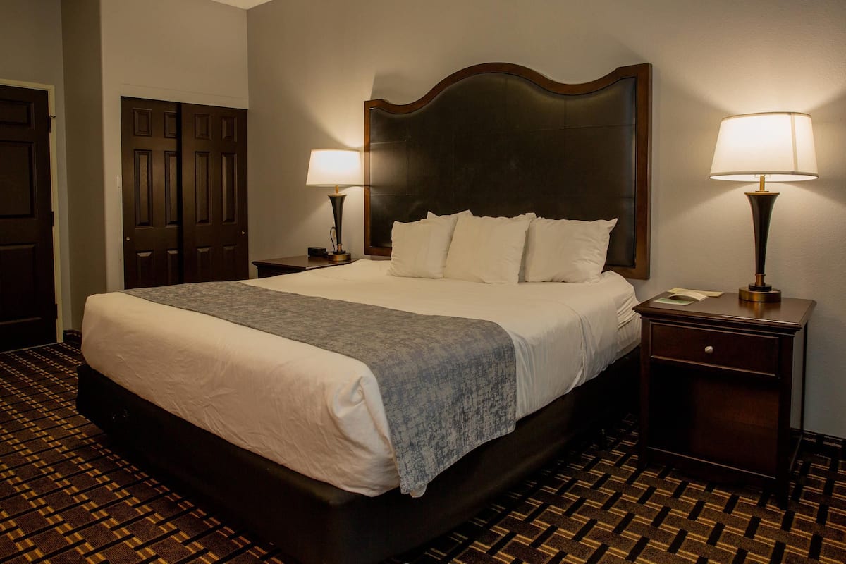 A hotel room with a large bed, two bedside tables with lamps, a wooden headboard, and a patterned carpet.